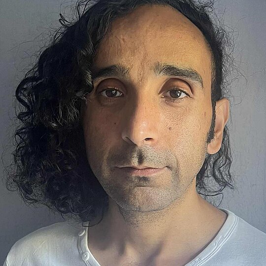 A man in a white shirt with long dark hair.