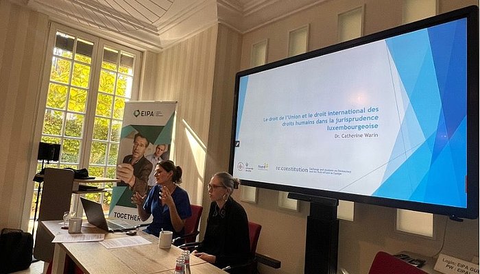 Photo of a panel with two people in front of a large screen
