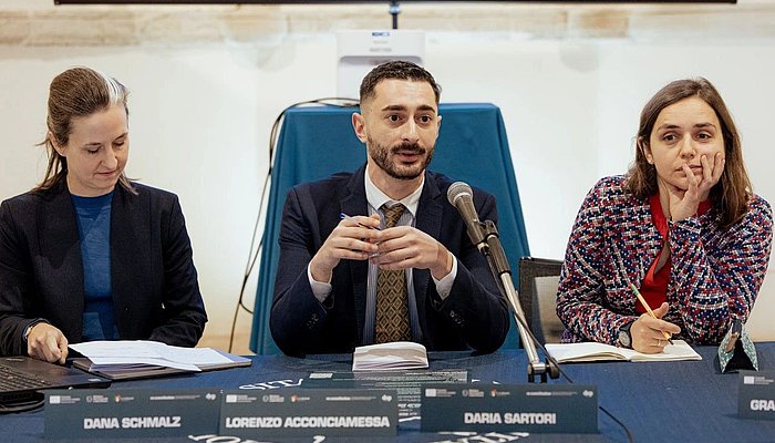 Three people, two women and a man, sitting on a panel, the man in the middle is speaking