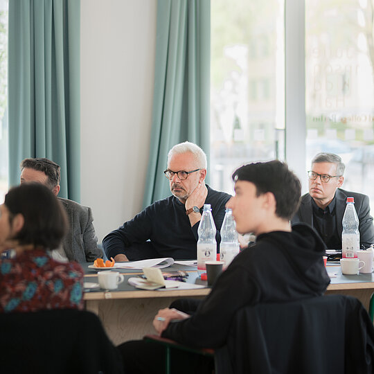 A group of people sitting at a table, listening to a speaker outside of the frame.