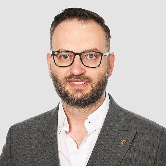 A man with short hair and glasses wearing a suit.
