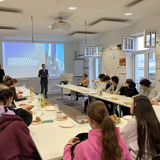 A group of students sitting in a seminar room while a woman presents in the front.