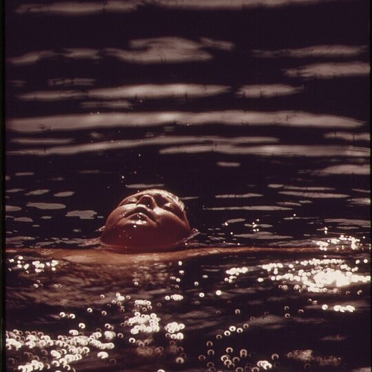 A person swimming in a lake, eyes closed.