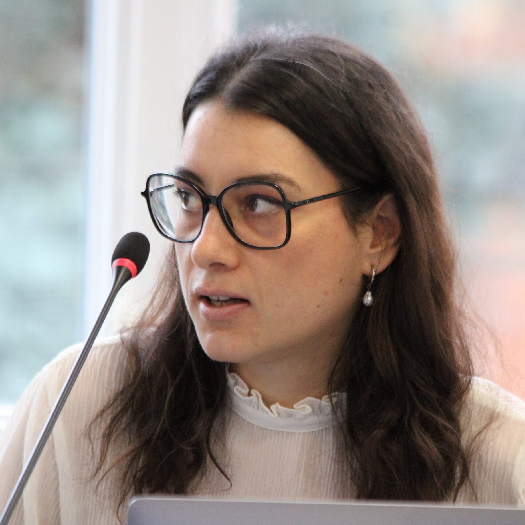 a woman with dark long hair wearing glasses is talking to a microphone.