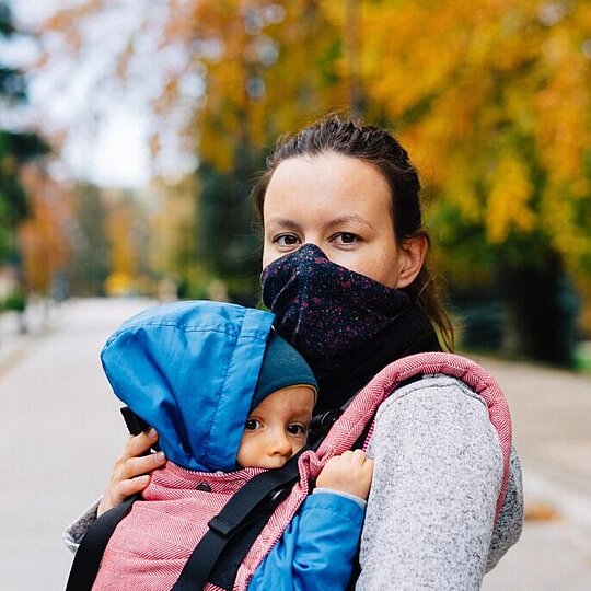 A young mother holding her child, the woman is wearing a mask.